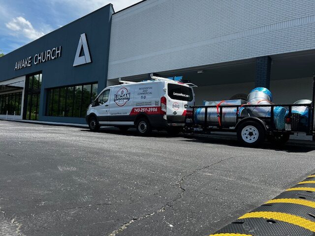 Lucsan van and a trailer loaded with spiral duct outside a commercial church building